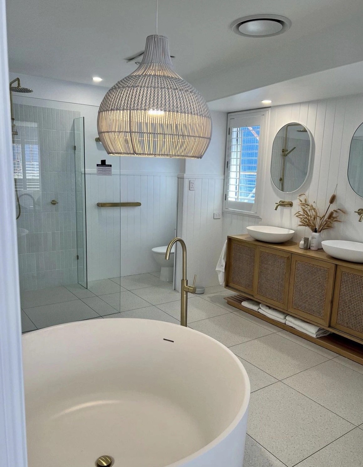 JL Coastal Projects completed an elegant bathroom renovation with brass accents, floating vanity, and spacious shower area.